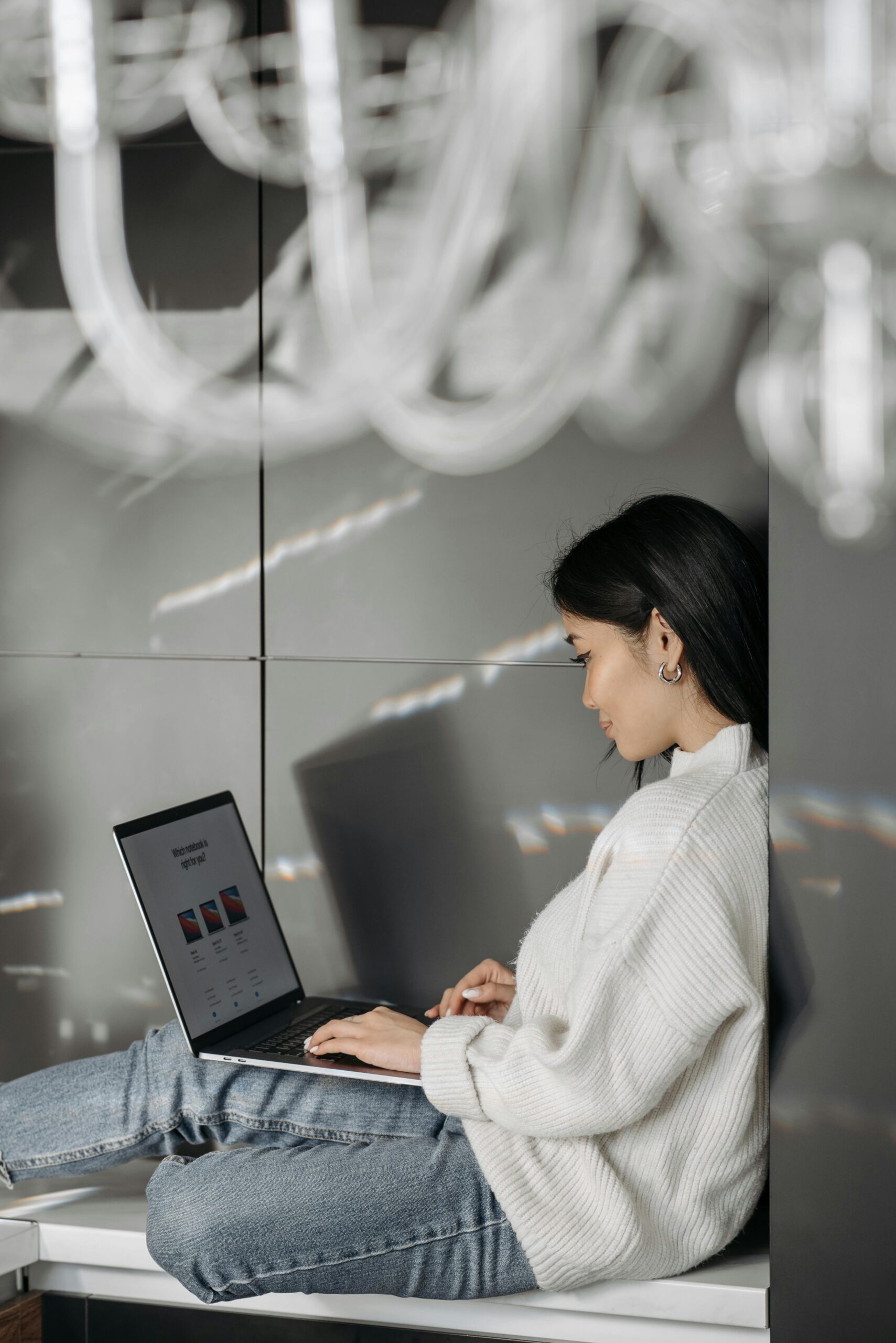 Young Asian woman focused on work using a laptop indoors, relaxed and engaged.